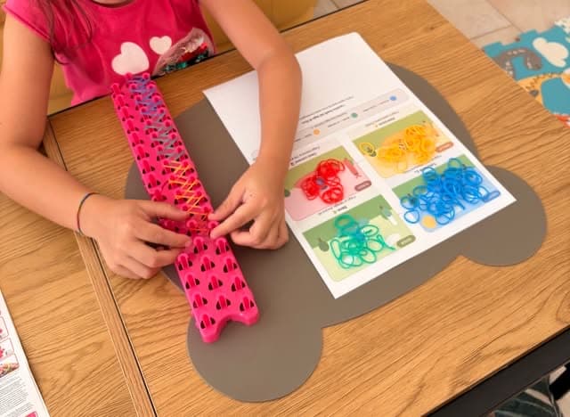 Le mani di una bambina che intreccia un braccialetto di elastici colorati durante un incontro in studio
